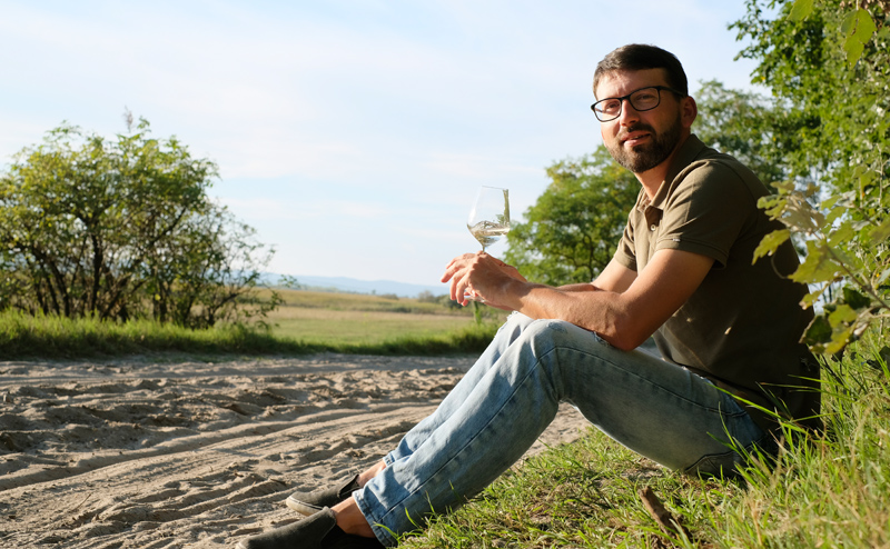 Michael Nekowitsch mit Weinglas in einer Riede in Illmitz am Boden sitzend