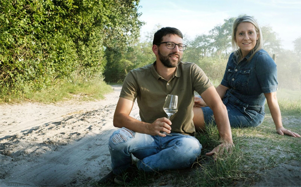 Michael und Elisabeth Nekowitsch mit Weinglas im Weingarten am Boden sitzend